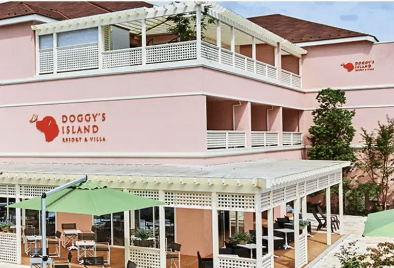 Exterior of Doggy's Island Japan resort, a pink building with a bright red sign and green patio umbrellas. 

