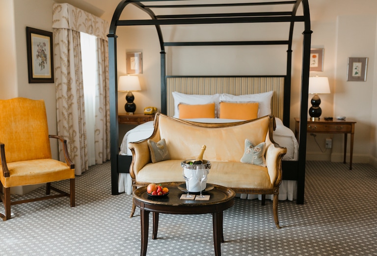 A room set up as a honeymoon suite at L'Auberge Carmel with a bed in the middle, two nightstands, and a sitting area with two glasses and the champagne bottle in the ice bucket.