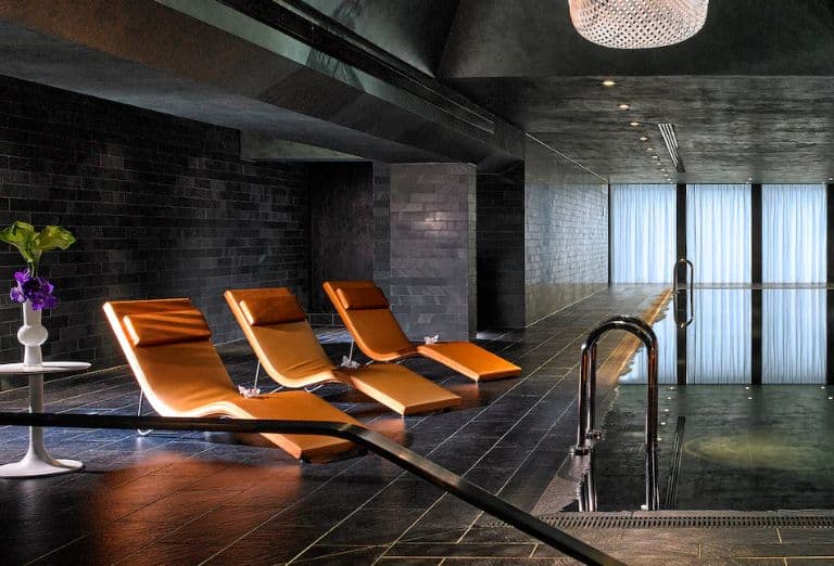Modern-designed spa in low lighting with orange lounge chairs, a pool