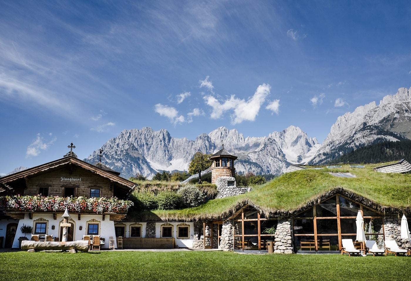 An exterior shot of the resort in the spring, rich with flowers and greenery, the Wilder Kaiser mountain range in the background
