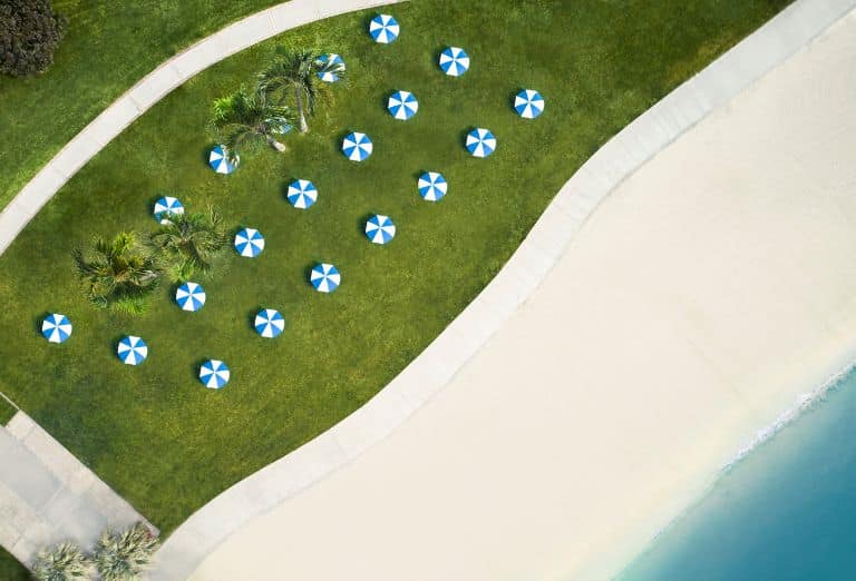A birdseye view of blue and white beach umbrellas on a lawn overlooking a beach and a bay