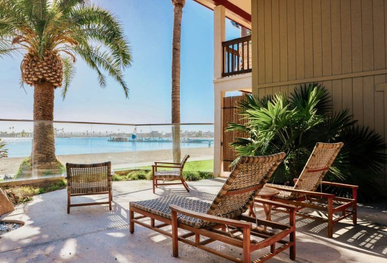 A balcony with wicker furniture shaded by a palm tree overlooking the beach