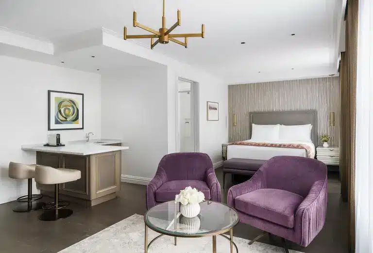 Junior Queen Suite at The Wallace Hotel, NYC, showcasing plush purple chairs, a modern kitchenette, and a queen-sized bed, as featured on Journey Beyond Aspen.