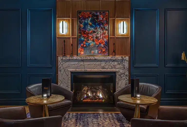 Cozy lounge area at The Wallace Hotel, NYC, with dark blue paneled walls, leather chairs, a marble fireplace, and vibrant artwork, as featured on Journey Beyond Aspen.