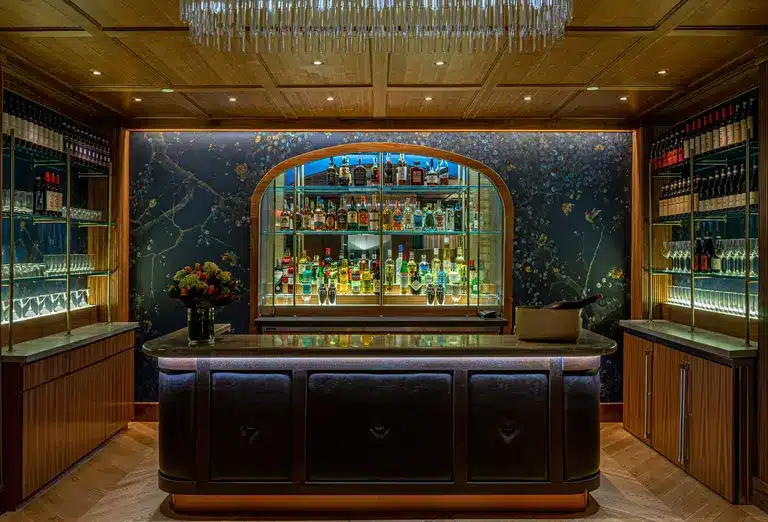 The bar area inside The Wallace Lounge, featuring an arched display of diverse spirits, warm wood tones, and a chic marble backdrop, highlighted on Journey Beyond Aspen.