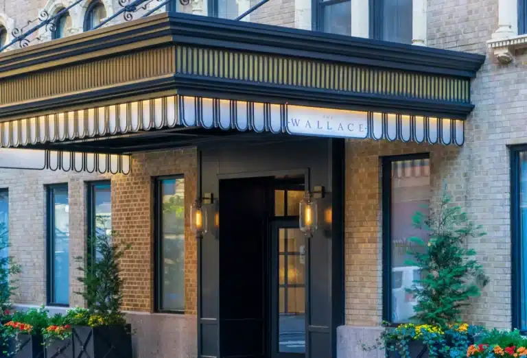 The Wallace Hotel entrance in NYC, featured on Journey Beyond Aspen, with a black and gold awning, illuminated signage, and welcoming lanterns.