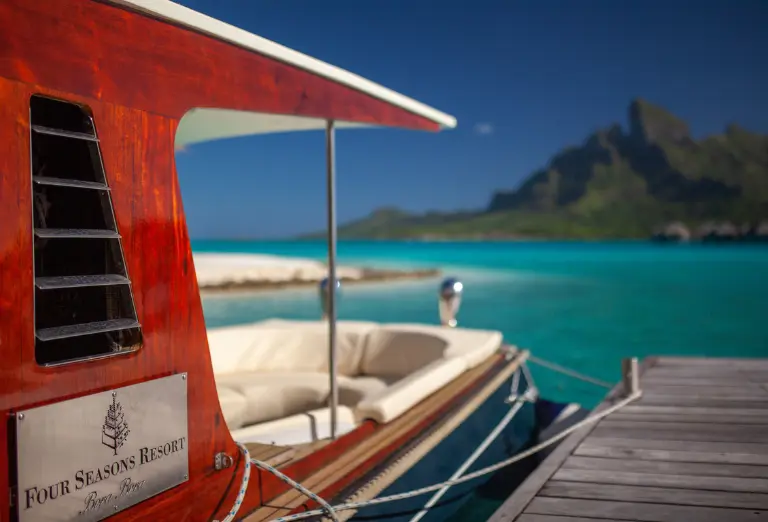 A luxury boat from the Four Seasons Resort Bora Bora docked against the backdrop of crystalline waters and the iconic Mount Otemanu, symbolizing the adventure and exclusivity offered by the resort.