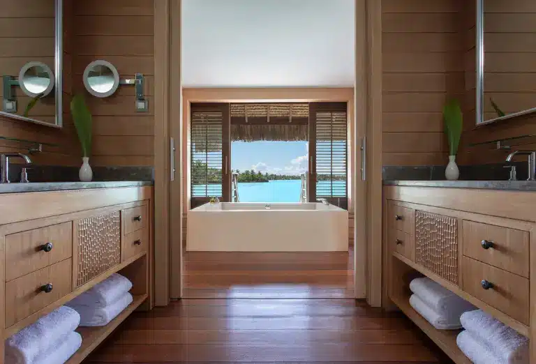 Elegant wooden bathroom interior in a Four Seasons Bora Bora villa, with a soaking tub overlooking the lagoon, dual vanity sinks, mirrors, and neatly placed towels.