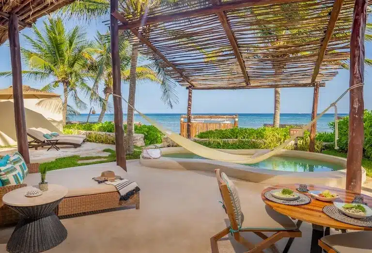 A spacious and inviting Bungalow Suite at the Viceroy Riviera Maya, with a covered patio featuring a hammock and dining area, overlooking the turquoise Caribbean Sea and lush tropical surroundings.