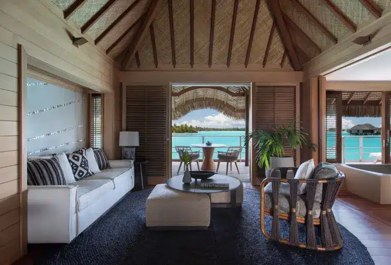 Luxurious living room of a Four Seasons Bora Bora villa with elegant furnishings and direct views of the turquoise lagoon through large windows, embodying tropical luxury.