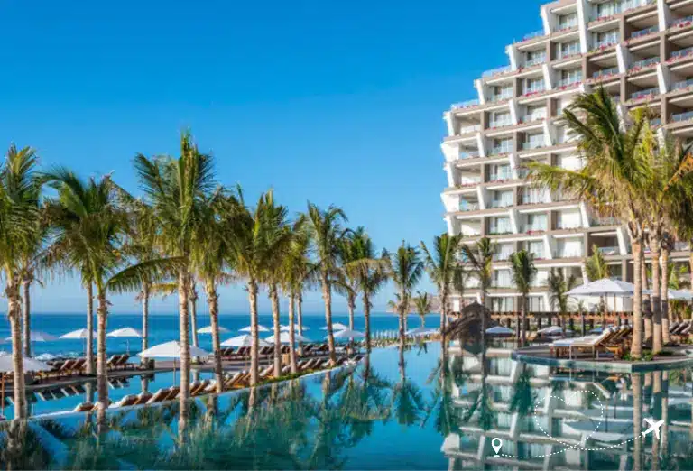 Grand Velas Los Cabos resort featuring a stunning infinity pool lined with palm trees, overlooking the ocean under a clear blue sky