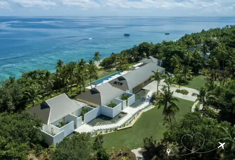 Aerial view of Vomo Island Resort in Fiji, showcasing modern white villas surrounded by lush tropical greenery and a turquoise sea.