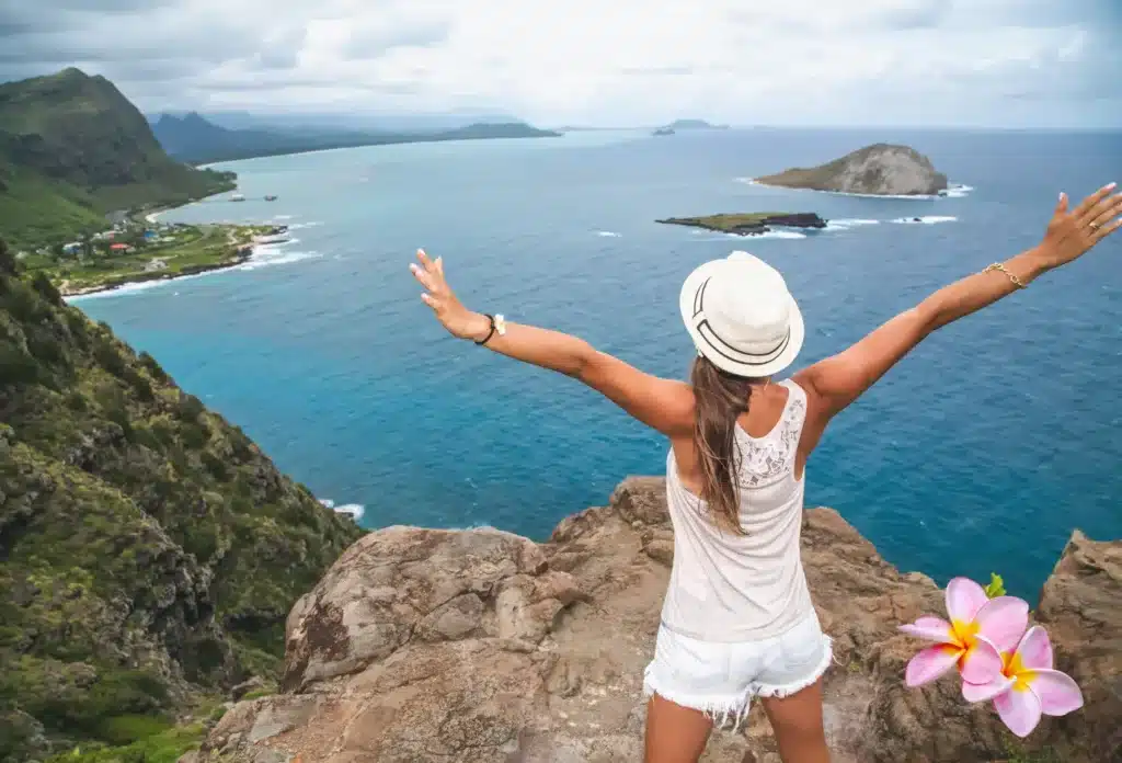 Woman on a cliff overlooking the Hawaiian coastline, representing the best time to visit Hawaii – featured on Journey Beyond Aspen.