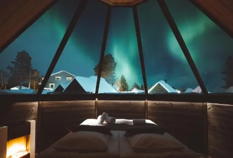 Bedroom at Apukka Resort in Finland with panoramic windows showcasing the Northern Lights.